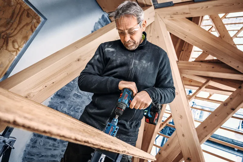 En person iført sikkerhedsudstyr borer i træ med en akku-boremaskine.